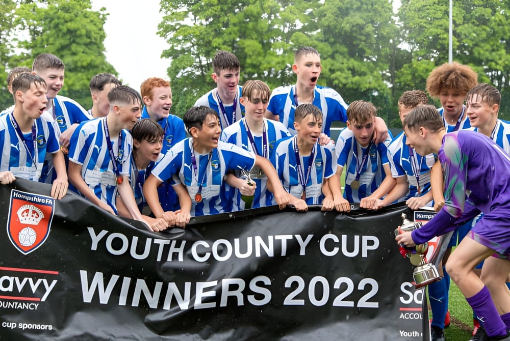 Eine Gruppe von Schülern der Corfe Hills School steht auf einem Rasenfeld um ein Banner zum Gewinn des Youth County Cup 2022.