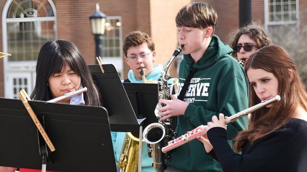 Schüler der Corfe Hills School spielen im Freien verschiedene Musikinstrumente und lesen Noten vor einem Backsteingebäude.