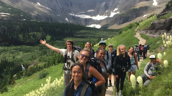 Schüler der Corfe Hills School wandern auf einem Pfad in einer bergigen Landschaft mit grüner Vegetation und Felsen im Hintergrund.