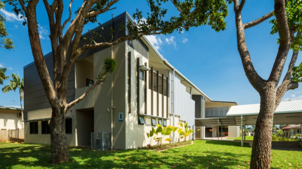 Das moderne zweistöckige Gebäude der Cornafulla National School ist von grünen Bäumen umgeben unter klarem blauem Himmel.