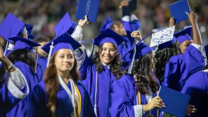 Absolventinnen und Absolventen der Cornafulla National School in lila Talaren mit Diplomen stehen gemeinsam im Freien.
