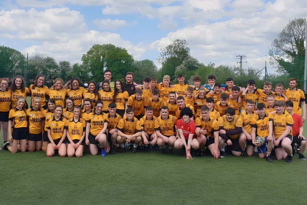 Eine große Gruppe von Schülerinnen in gelben Uniformen posiert für ein Gruppenfoto auf dem Rasen der Cornafulla National School.