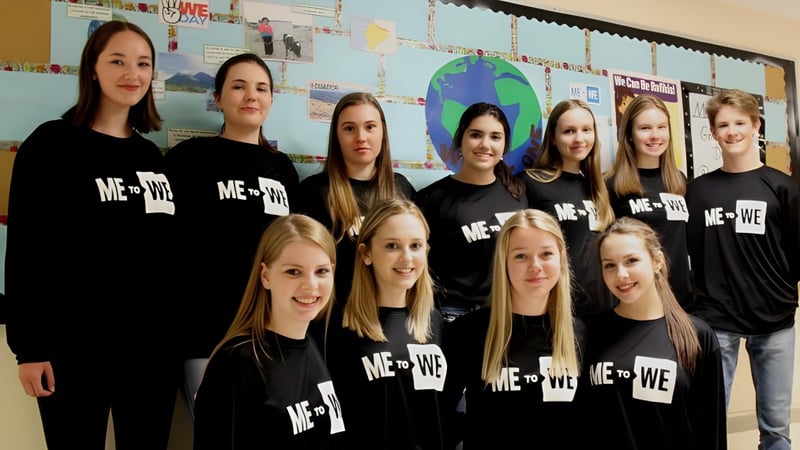 Eine Gruppe Schülerinnen mit schwarzen ME + WE-Shirts steht vor einer mit Lernmaterialien bedeckten Wand in der Corner Brook Regional High School.