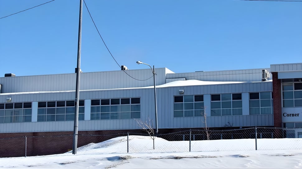 Das große Industriegebäude auf dem Gelände der Corner Brook Regional High School bei klarem Himmel und Schnee im Vordergrund.