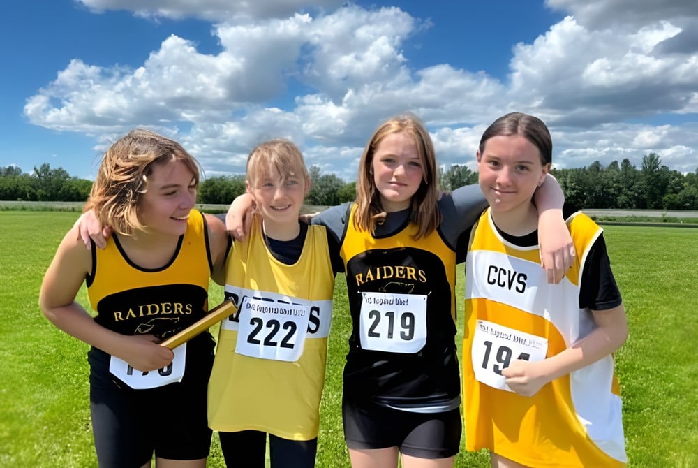 Vier junge Athletinnen in gelb-schwarzen Trikots stehen auf dem Sportfeld der Cornwall Collegiate & Vocational School unter bewölktem Himmel.
