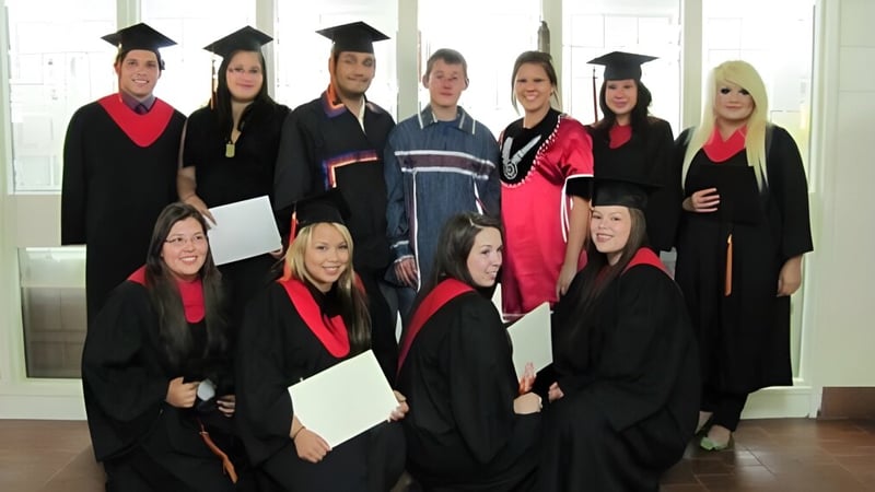 Eine Gruppe von Absolventinnen und Absolventen der Cornwall Collegiate & Vocational School posiert in akademischer Kleidung vor großen Fenstern.