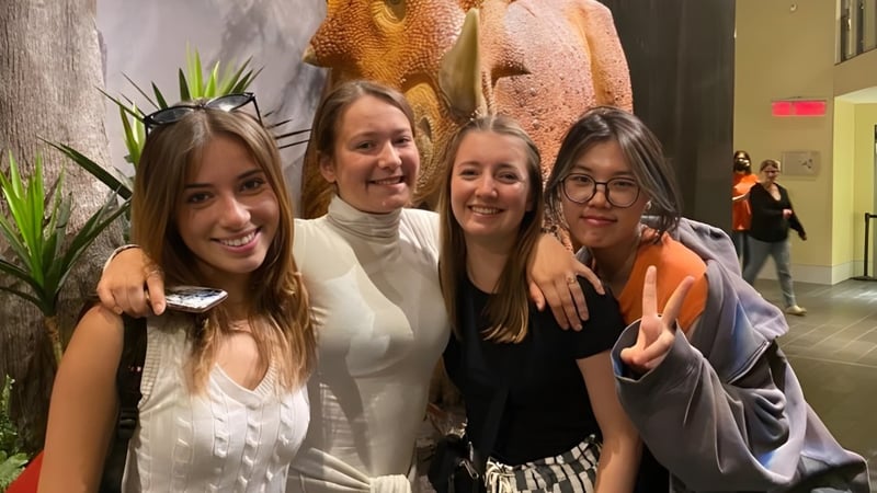 Vier Schülerinnen der Cornwall Collegiate & Vocational School posieren zusammen vor bunten Kunstwerken im Innenraum.