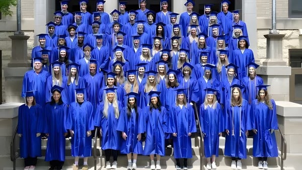 Eine große Gruppe von Absolventinnen und Absolventen der Cotter Schools steht in blauen Talaren und Hüten auf den Stufen eines Gebäudes mit steinerner Fassade.