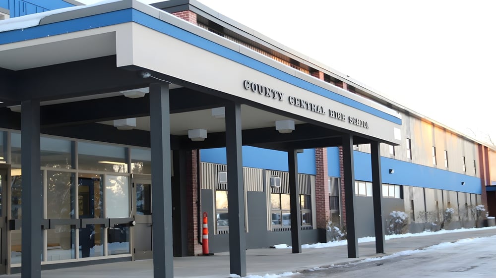 Das moderne mehrstöckige Gebäude der County Central High School steht bei winterlichem Schnee mit einem überdachten Eingang.