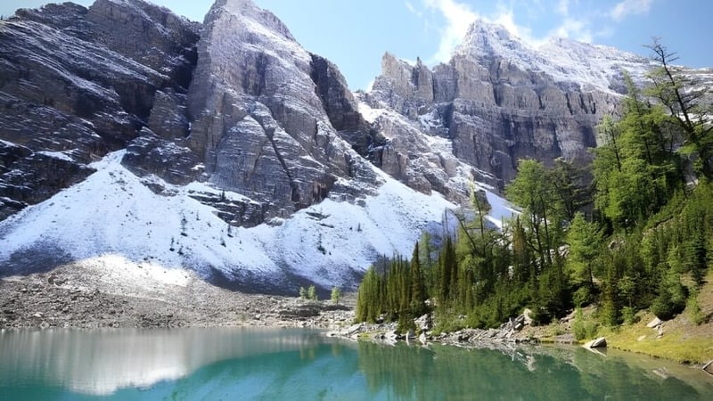 Ein türkisblauer See mit schneebedeckten Bergen und immergrünen Bäumen im Vordergrund nahe der County Central High School.