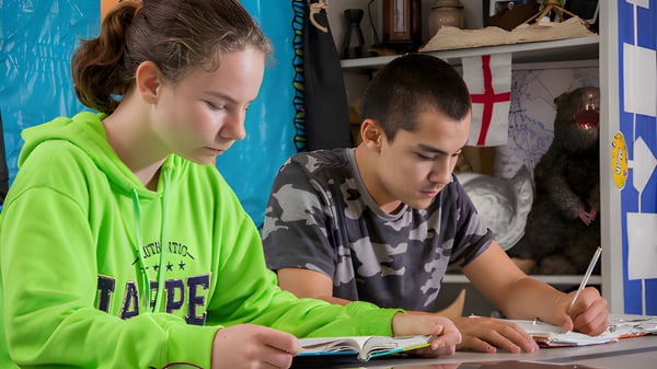 Zwei Schüler der Covenant Christian School lesen und schreiben konzentriert in einem gemütlichen Innenraum.