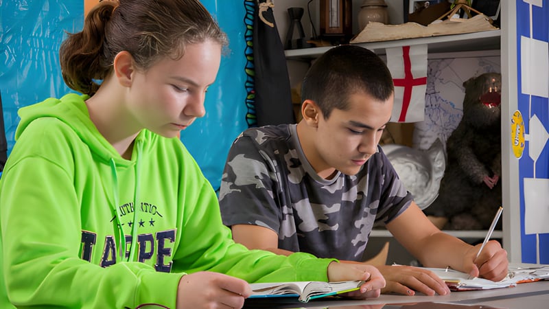 Zwei Schüler der Covenant Christian School lesen und schreiben konzentriert in einem gemütlichen Innenraum.