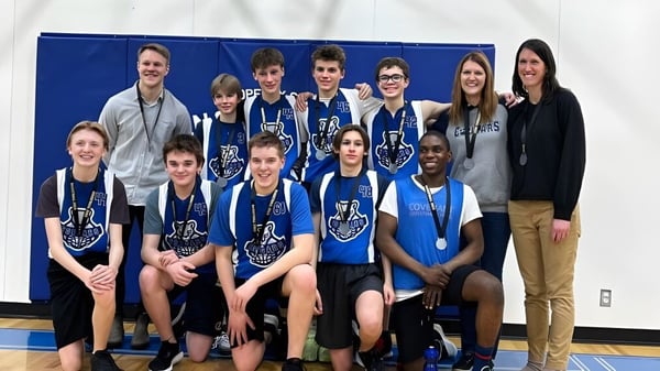 Eine Gruppe Schüler der Covenant Christian School posiert gemeinsam als Sportteam in einer Turnhalle vor blauem Hintergrund.