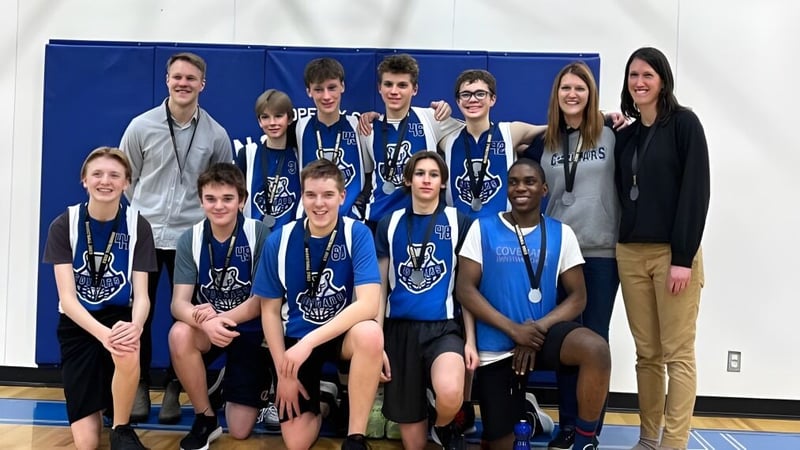 Eine Gruppe Schüler der Covenant Christian School posiert gemeinsam als Sportteam in einer Turnhalle vor blauem Hintergrund.