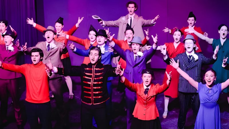 Schüler der Covenant Day School führen eine lebhafte Bühnenaufführung in bunten Kostümen mit erhobenen Armen auf.