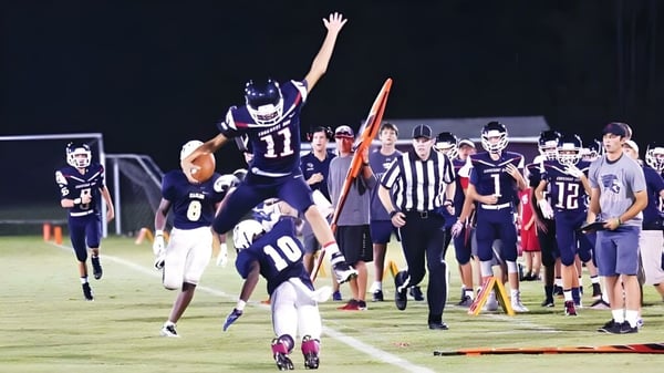 Fußballspieler, Schiedsrichter und Zuschauer auf dem Spielfeld der Covenant Day School, ein Spieler feiert mit erhobenen Armen.