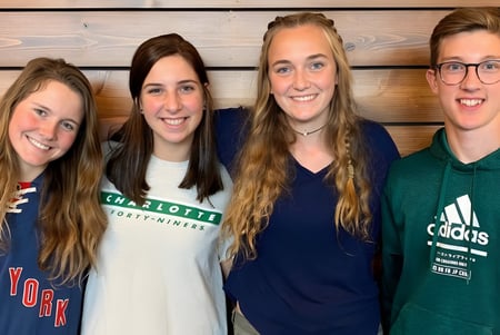 Vier Schülerinnen der Covenant Day School stehen lächelnd vor einer Holzvertäfelung.