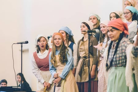 Eine Gruppe junger Frauen steht mit Mikrofonen auf der Bühne der Covenant High School bei einer Aufführung.