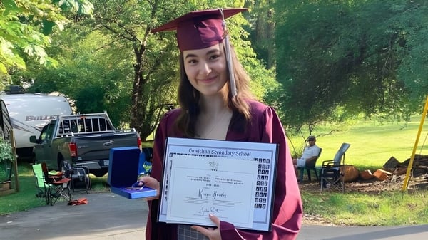 Eine Absolventin der Cowichan Secondary School steht im Freien mit ihrem Diplom in der Hand.