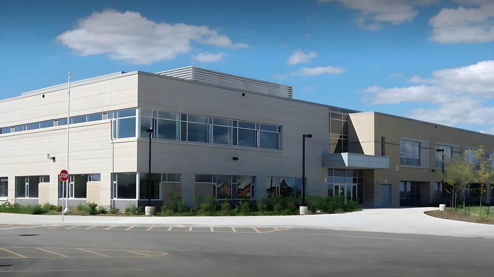 Das moderne mehrstöckige Gebäude der Craig Kielburger Secondary School mit großen Fenstern steht auf einem gepflasterten Parkplatz unter blauem Himmel.