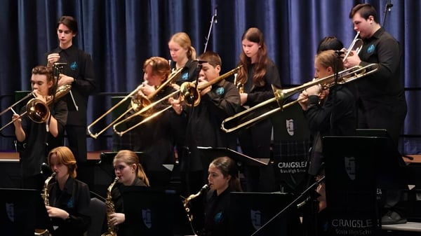 Eine Gruppe Schülerinnen und Schüler der Craigslea State High School spielt auf der Bühne vor einem dunklen Vorhang verschiedene Instrumente.