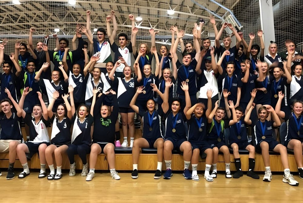 Eine Gruppe Schüler der Craigslea State High School posiert gemeinsam in der Sporthalle mit erhobenen Armen.