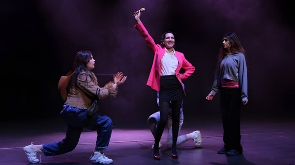 Drei Personen, darunter Schülerinnen und Schüler, stehen auf der Bühne des Cranbrook Education Campus in einer dunklen Szene.