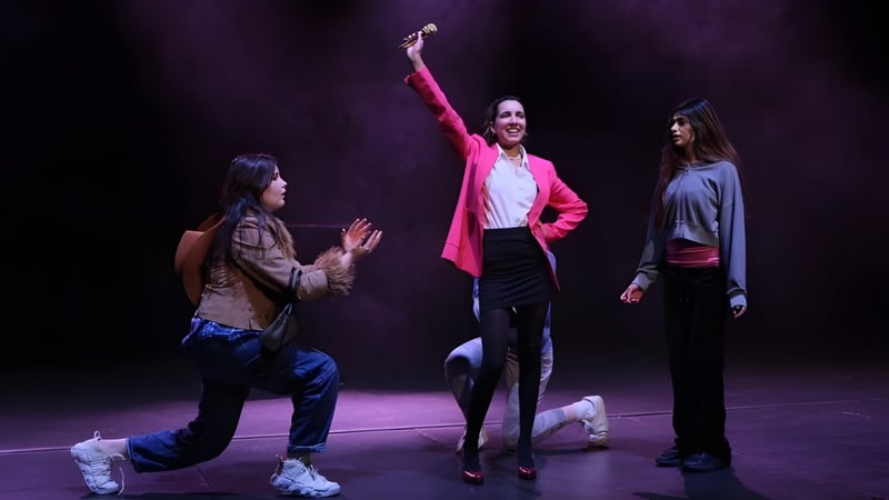 Drei Personen, darunter Schülerinnen und Schüler, stehen auf der Bühne des Cranbrook Education Campus in einer dunklen Szene.