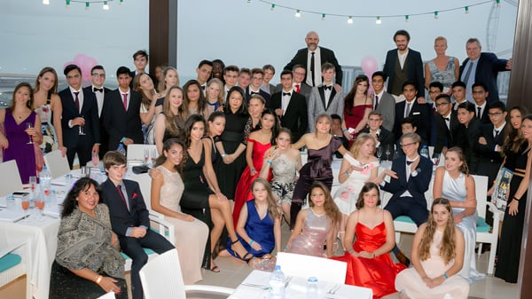 Eine Gruppe von Personen in formeller Kleidung versammelt sich bei einer Feier am Cranbrook Education Campus unter Lichterketten.
