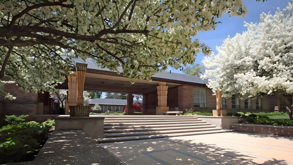 Das Backsteingebäude mit überdachtem Eingang der Cranbrook Schools ist von blühenden Bäumen und einem gepflasterten Weg umgeben.