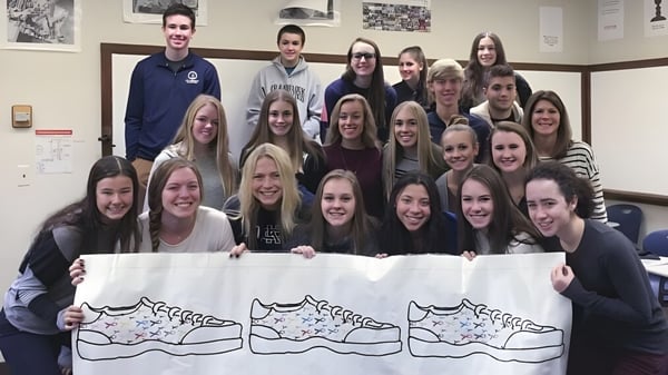 Eine Gruppe von Schülerinnen und Schülern der Cranbrook Schools hält in einem Innenraum ein großes Banner mit einer Katzenzeichnung.