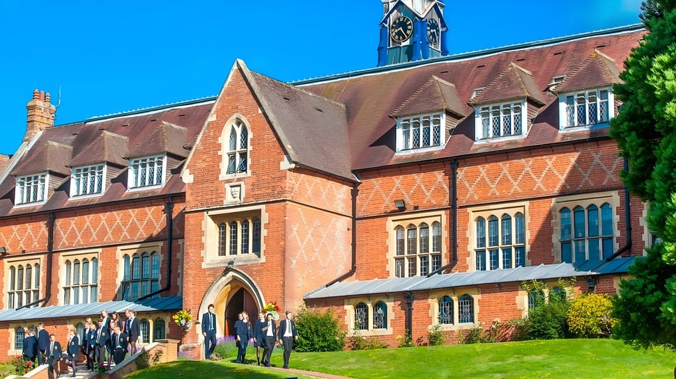 Das historische Backsteingebäude der Cranleigh School steht in einer Grünanlage mit Schülerinnen und Schülern im Vordergrund.