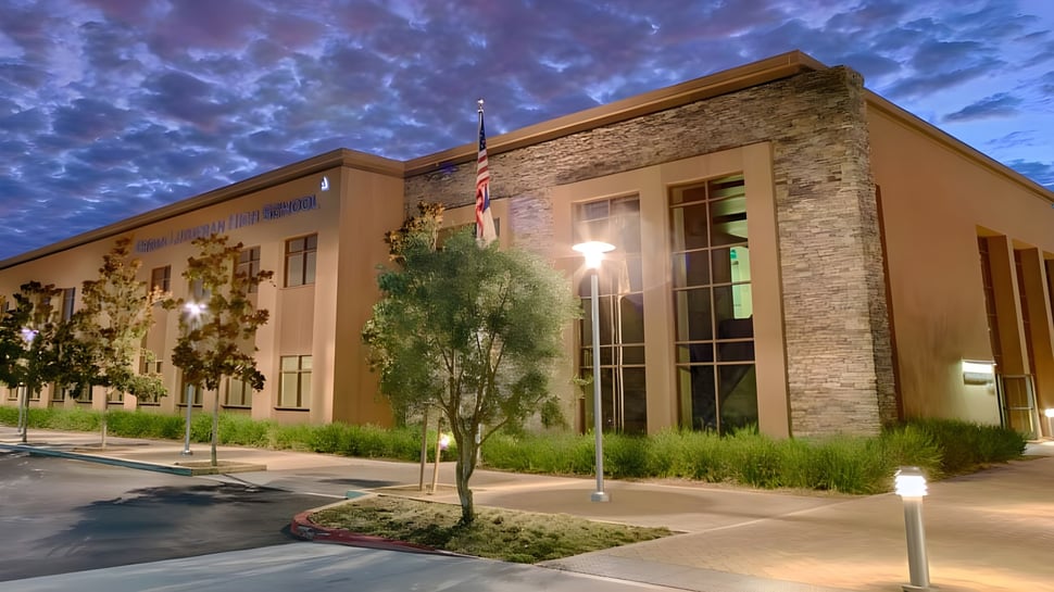 Das moderne mehrstöckige Gebäude mit Steinfassade der Crean Lutheran High School steht vor bewölktem Himmel und ist von Grün umgeben.