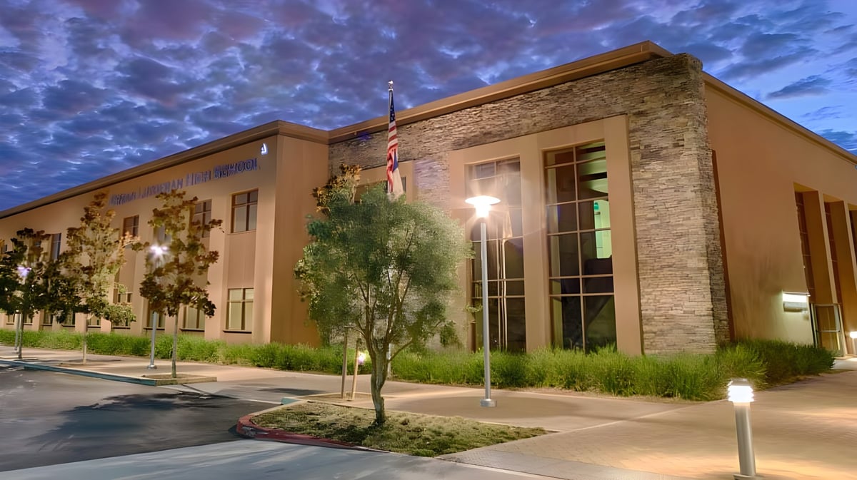 Das moderne mehrstöckige Gebäude mit Steinfassade der Crean Lutheran High School steht vor bewölktem Himmel und ist von Grün umgeben.