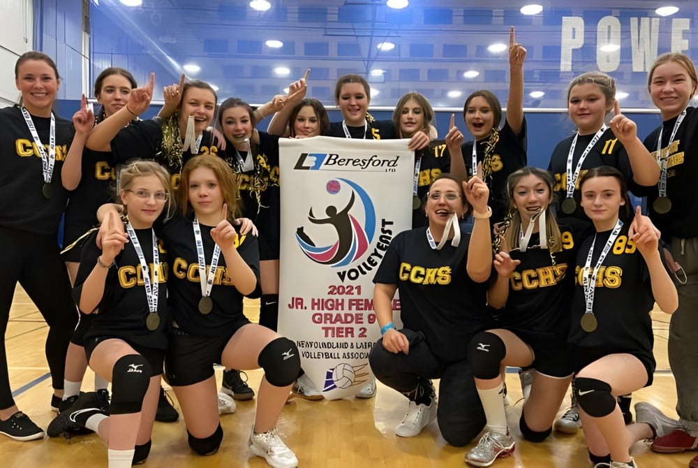 Eine Gruppe junger Volleyballspielerinnen des Crescent Collegiate hält in der Sporthalle ein Banner mit dem Beresford-Logo.