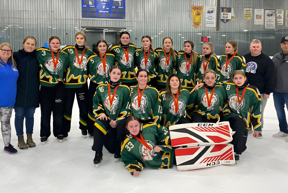 Eine Gruppe junger Hockey-Spielerinnen in grünen und orangen Trikots auf dem Eis der Crescent Heights High School.