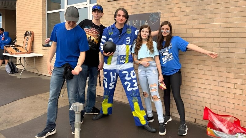 Eine Gruppe Schülerinnen und Schüler der Crescent Heights High School steht in Sporttrikots vor einem Backsteingebäude.