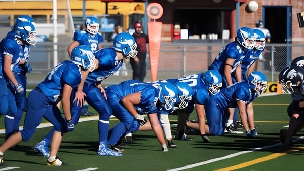 Schüler der Crescent Heights High School versammeln sich in blauen Trikots auf dem Fußballfeld mit einem Gebäude im Hintergrund.