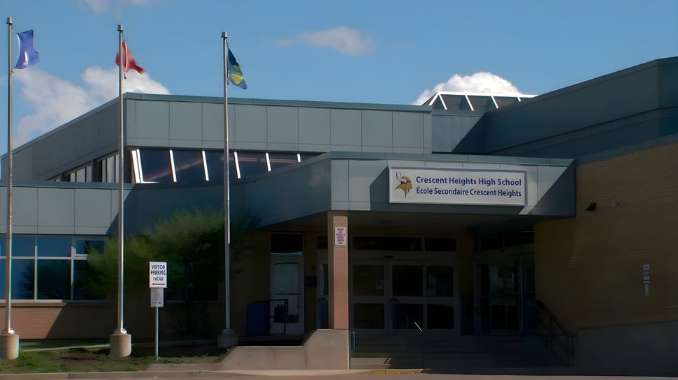 Das moderne mehrstöckige Schulgebäude der Crescent Heights High School mit wehenden Flaggen auf dem Dach ist zu sehen.