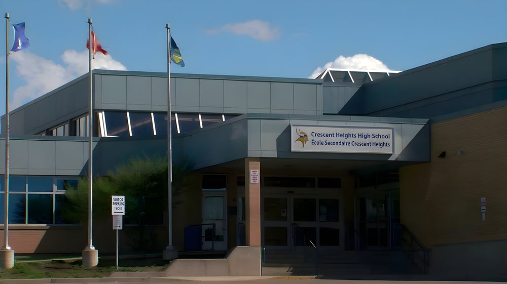 Das moderne mehrstöckige Schulgebäude der Crescent Heights High School mit wehenden Flaggen auf dem Dach ist zu sehen.