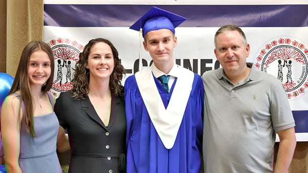 Eine Gruppe von vier Personen posiert bei der Abschlussfeier auf dem Campus der Creston Valley Secondary School mit einem jungen Mann in Talar und Mütze.