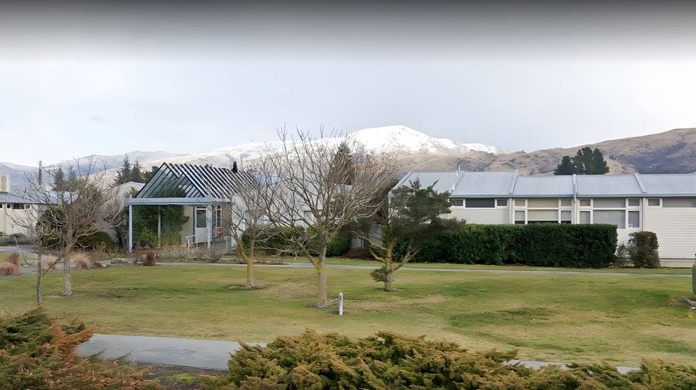 Ein Park mit Pavillon und Bäumen auf dem Gelände des Cromwell College vor schneebedeckten Bergen im Hintergrund.