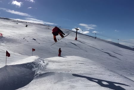 Schüler des Cromwell College fahren auf einer verschneiten Skipiste den Berg hinunter unter einem blauen Himmel mit vereinzelten Wolken.