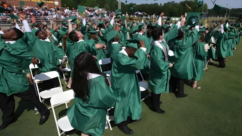 Eine große Gruppe von Schülern in grünen Abschlusstrachten versammelt sich auf einem Feld bei der Crowsnest Consolidated High School.