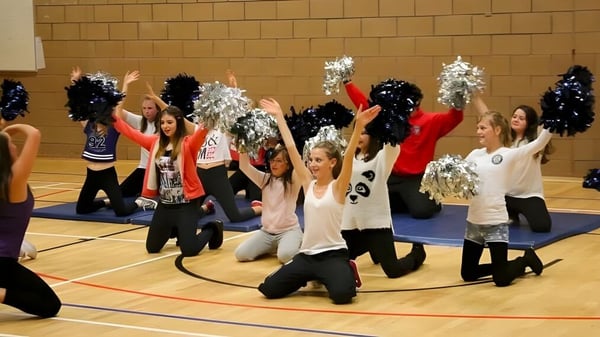 Eine Gruppe Cheerleader führt mit bunten Uniformen und Pompons auf dem Basketballfeld der Currie Community High School eine Show auf.