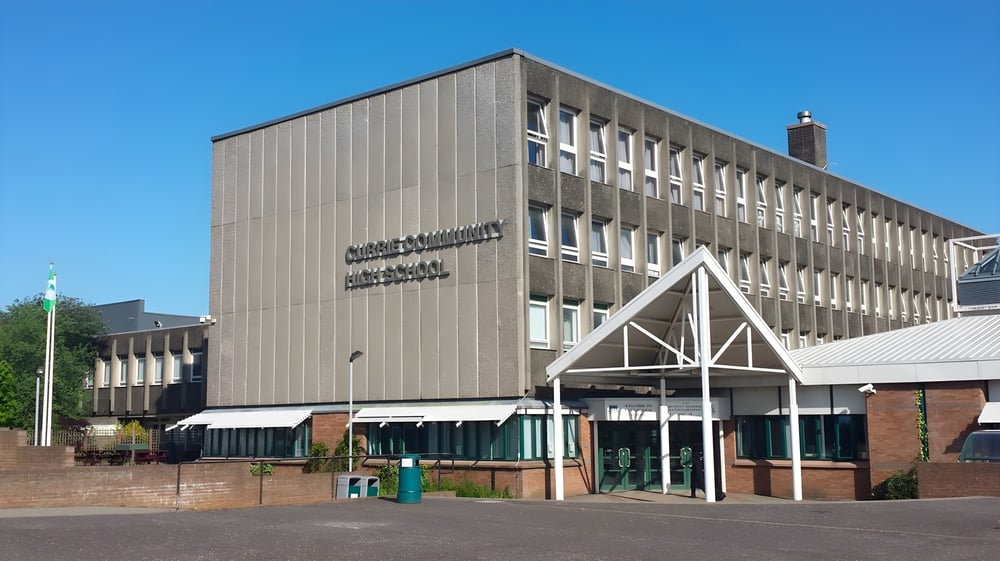 Das moderne Hauptgebäude der Currie Community High School mit angrenzendem gepflastertem Bereich und Grünflächen im Hintergrund.