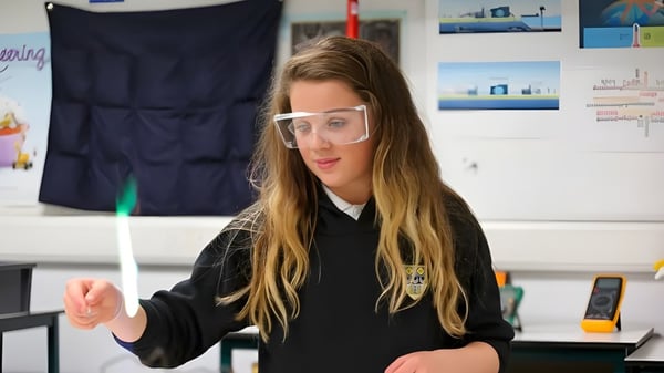 Eine Schülerin der Currie Community High School trägt eine Schutzbrille und steht in einem Klassenraum mit Bildungspostern.