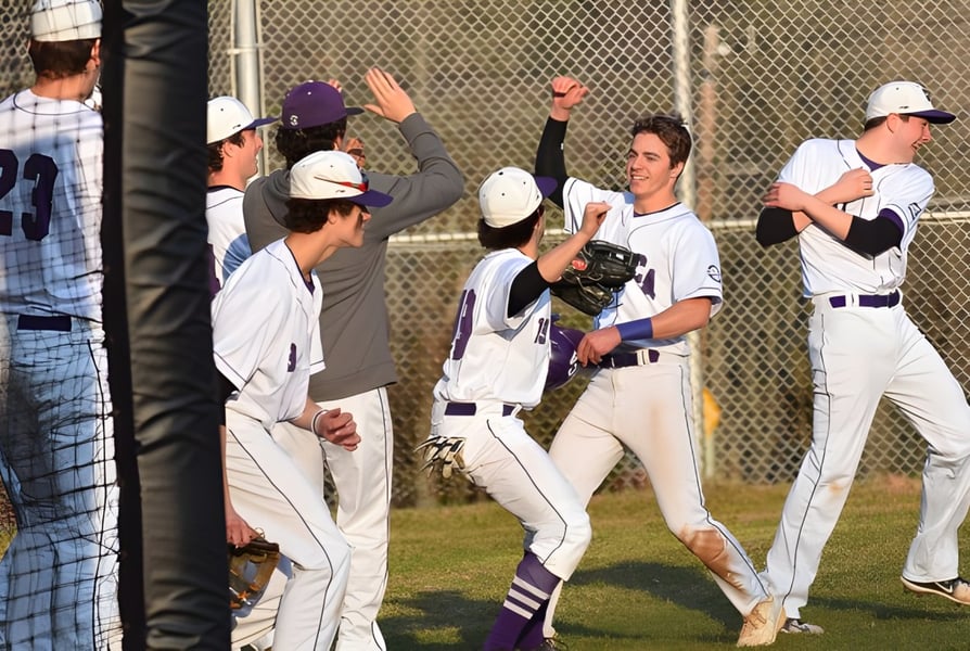 Schüler der Cushing Academy feiern gemeinsam auf dem Baseballfeld vor Zuschauern hinter dem Zaun.