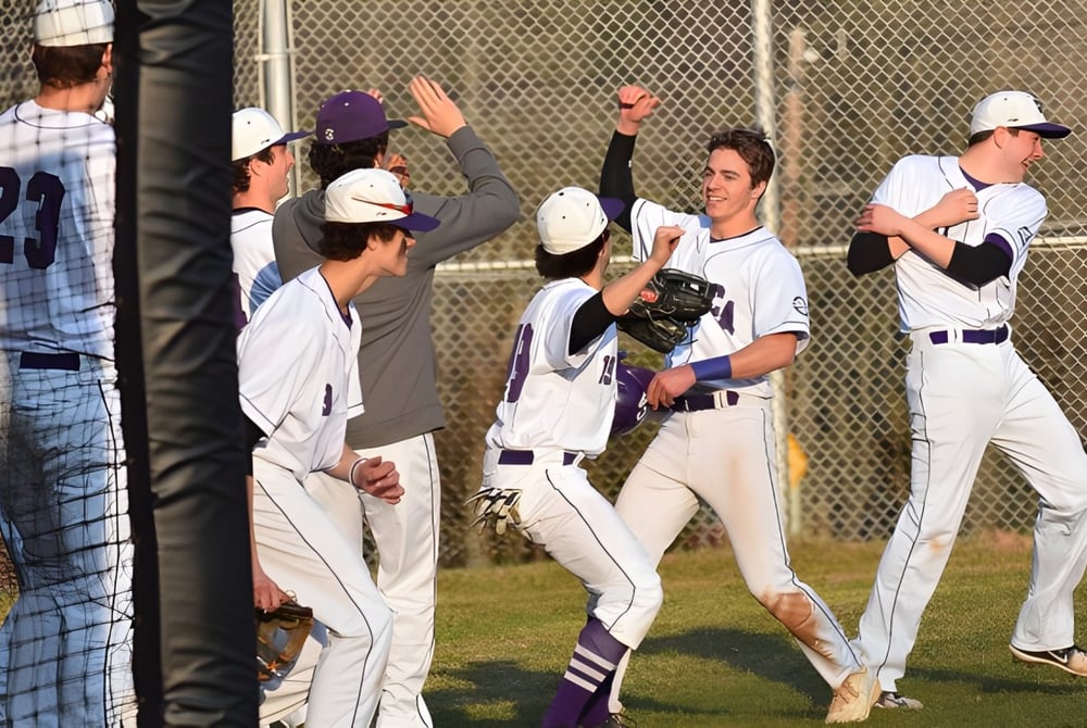 Eine Gruppe von Baseballspielern der Cushing Academy feiert auf dem Baseballfeld neben einem Zaun.