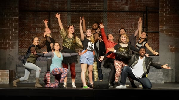 Eine Gruppe Schüler der Cushing Academy posiert vor einer Backsteinwand mit erhobenen Armen.